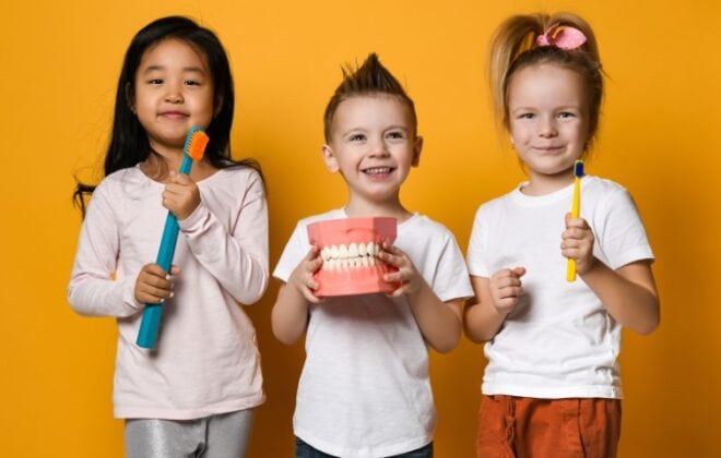 Happy children holding toothbrush and model teeth.