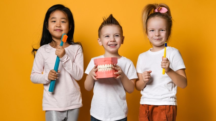 Happy children holding toothbrush and model teeth.