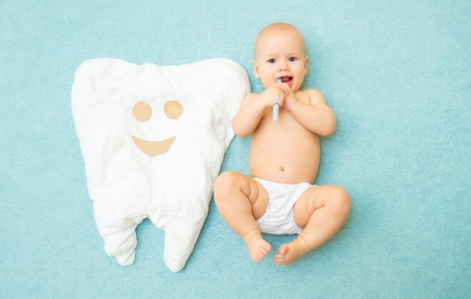Cute baby lies with a toothbrush on a blue background. White tooth made of fabric.